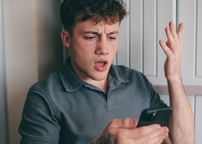 Young man reacting with frustration while looking at his phone, illustrating wedding vendors leaving bride with no cupcakes due to allergy Young man reacting with frustration while looking at his phone, illustrating wedding vendors leaving bride with no cupcakes due to allergy
