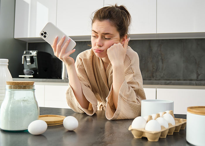 Bride with allergy looking disappointed while holding phone in kitchen, surrounded by baking ingredients, no cupcakes from wedding vendors. Bride with allergy looking disappointed while holding phone in kitchen, surrounded by baking ingredients, no cupcakes from wedding vendors.