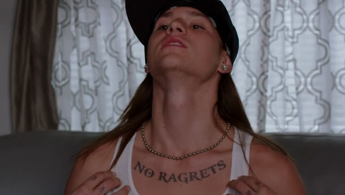 Person wearing a cap showing a large "NO RAGRETS" tattoo on their chest, illustrating strange tattoo mistakes refused by artists.