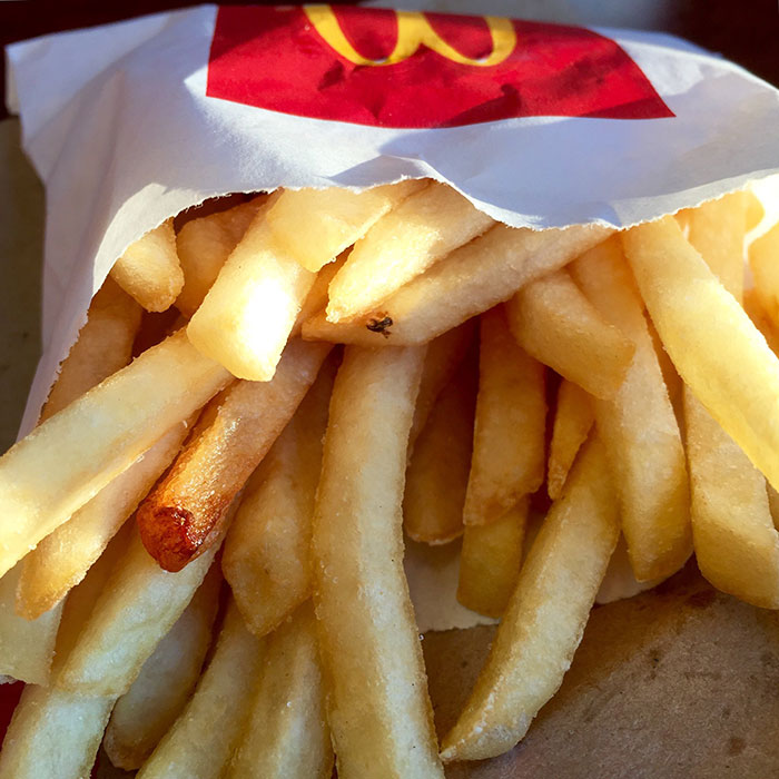 Close-up of fries in fast food packaging, highlighting man filming wife secretly to prove she eats his fries.