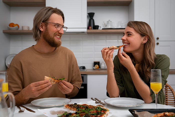 Couple enjoying pizza at home, laughing and sharing a meal, illustrating family drama over fries eating habits.