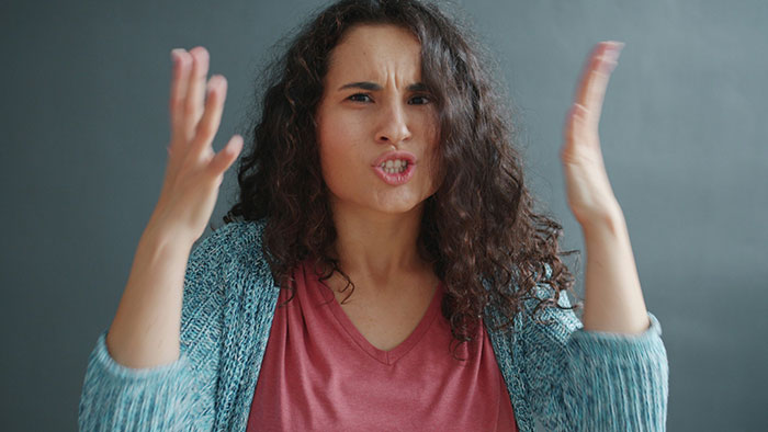 Woman with curly hair frustrated and gesturing, expressing anger over not affording her miracle baby or adoption refusal.