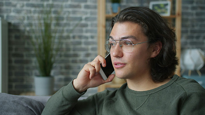 Young man with glasses making a phone call, reflecting on rejection and dating after being turned down thrice. Young man with glasses making a phone call, reflecting on rejection and dating after being turned down thrice.
