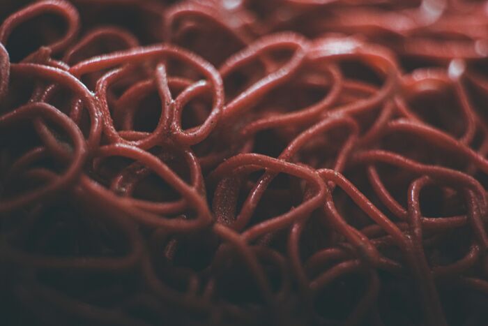 Close-up of a tangled mass of red spaghetti noodles, resembling an unusual shrimp jello texture and color.