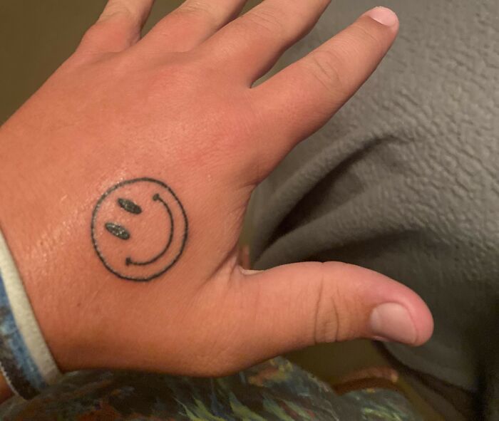 Hand with a small smiley face tattoo on the back, illustrating strange or refused tattoo artists' ink choices.
