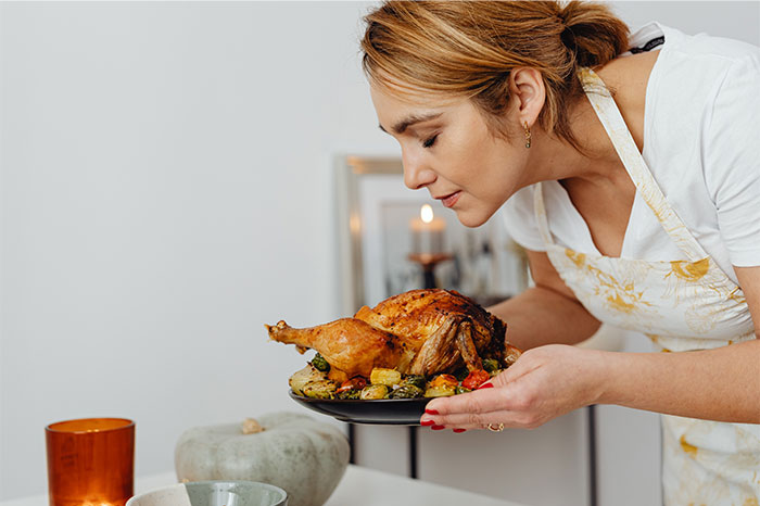 Woman in apron smelling a roasted chicken on a plate, showcasing a smart cooking cheat with blow drying chicken.