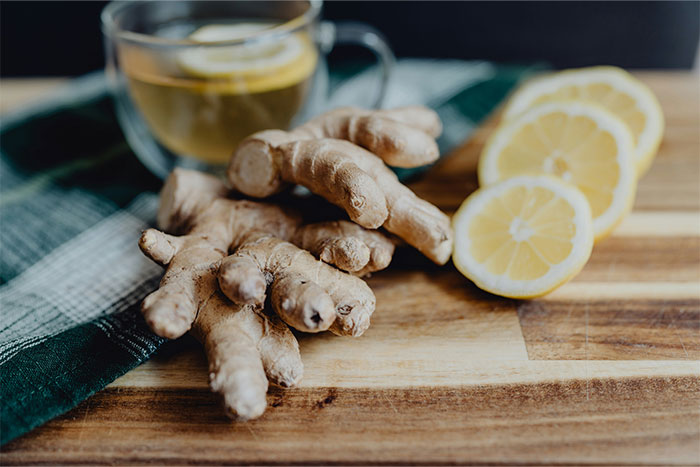 Fresh ginger roots and sliced lemons on a wooden board with a glass of tea, illustrating kitchen cheats for cooking smarter.