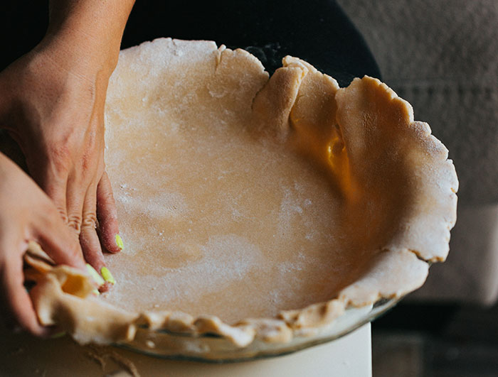 Hands shaping pie crust in a glass dish, demonstrating a simple kitchen hack for cooking smarter, not harder.