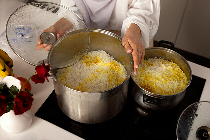 Person lifting lid off a large pot of cooked rice on stovetop, demonstrating cooking smarter kitchen cheats.