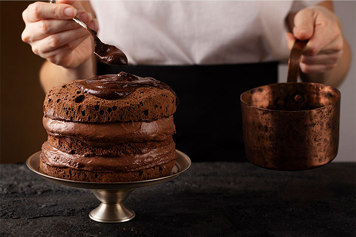 Person spreading chocolate frosting on a layered cake with a spoon, showcasing creative cooking and kitchen hacks.