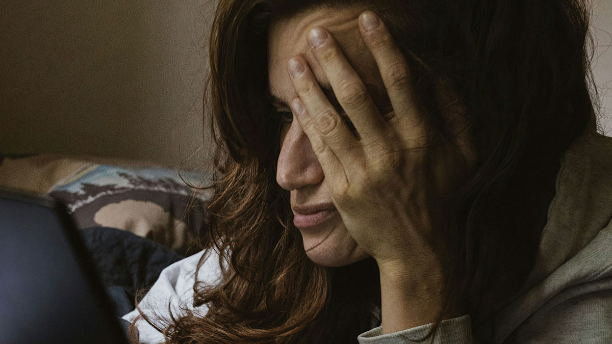 Woman hiding face with hand while looking at a screen, illustrating hilariously strange things people do when no one is watching.