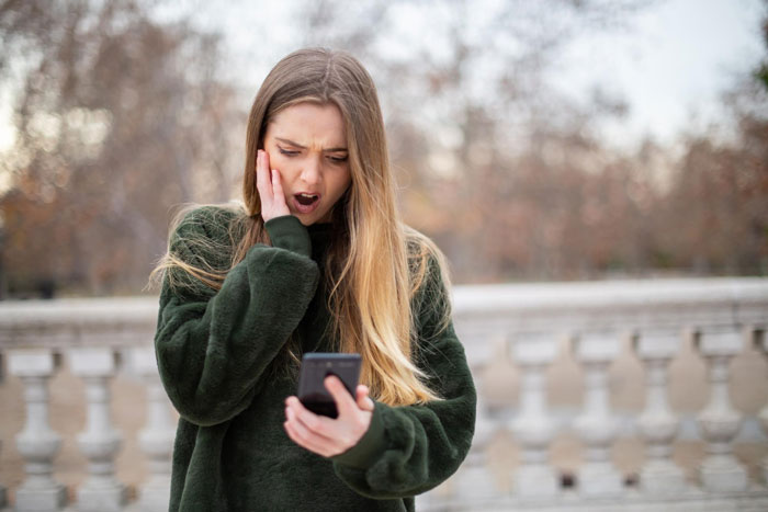 Young woman looking shocked and upset while reading on her smartphone outdoors, reflecting daughter calling husband a cheater. Young woman looking shocked and upset while reading on her smartphone outdoors, reflecting daughter calling husband a cheater.