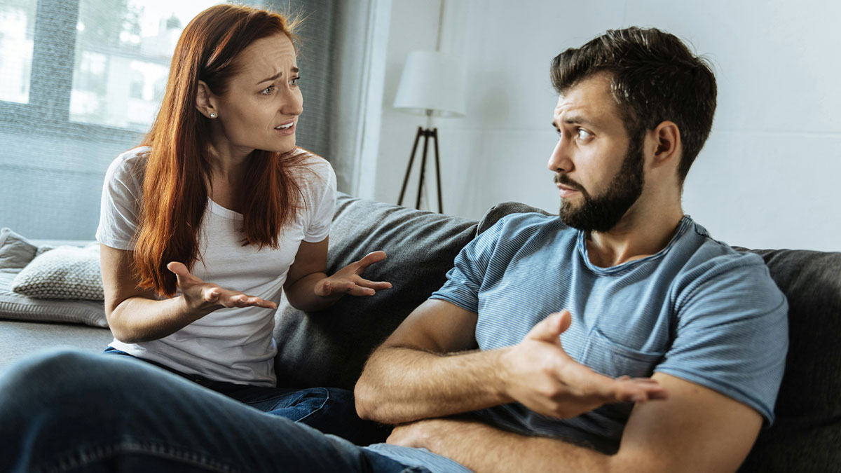 Couple sitting on a couch having an intense argument, illustrating MIL ruins birthday and DIL refuses celebrations.