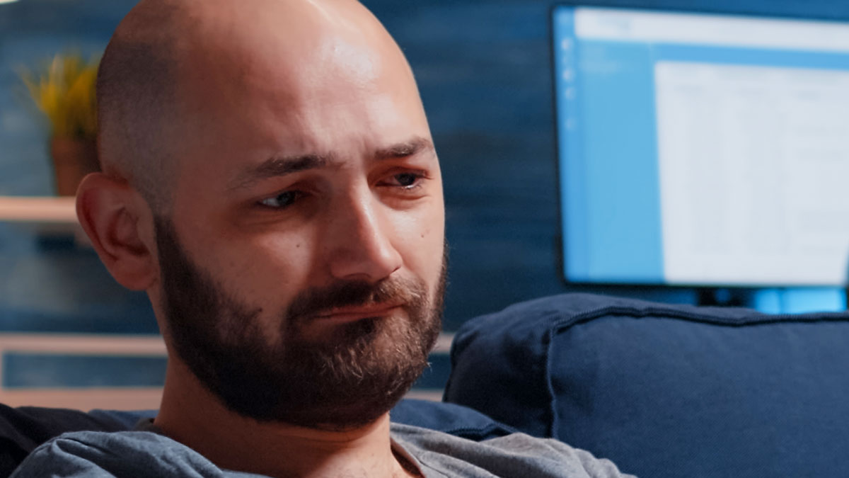Man looking upset sitting on couch, reflecting tension from argument and missed hospital calls from wife.