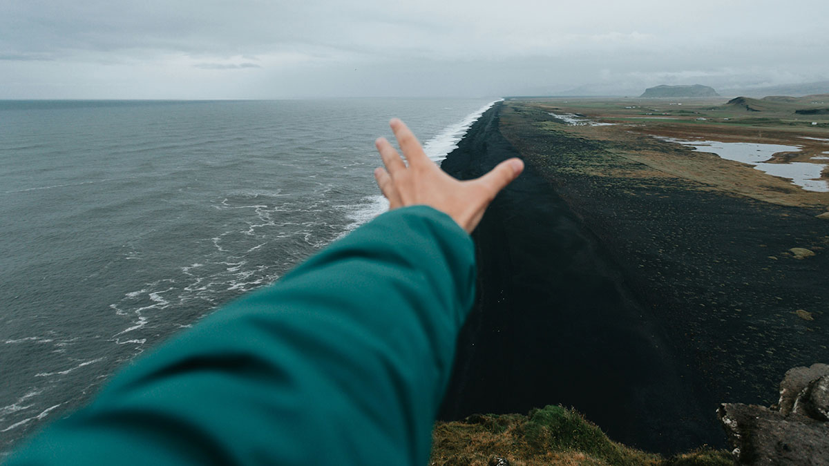 Person reaching out toward a coastline with black sand, capturing a moment of instant karma manifestation in nature.