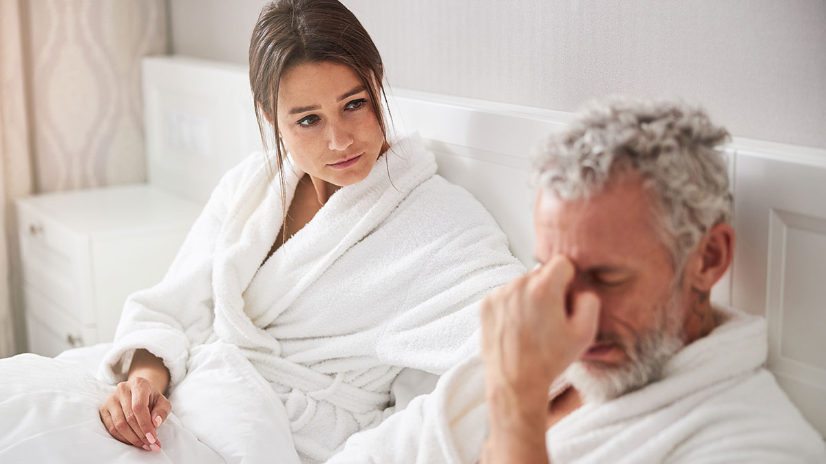 Woman in bathrobe talks to her boyfriend looking distressed, reflecting on a wake-up call involving his grown son.