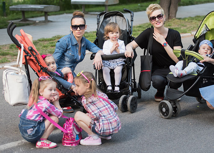 Two women with two kids each in strollers, struggling for support after surgery while caring for their children outdoors. Two women with two kids each in strollers, struggling for support after surgery while caring for their children outdoors.