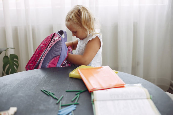 Young girl packing a backpack at a table with school supplies, reflecting a single mom’s plastic surgery support dilemma. Young girl packing a backpack at a table with school supplies, reflecting a single mom’s plastic surgery support dilemma.