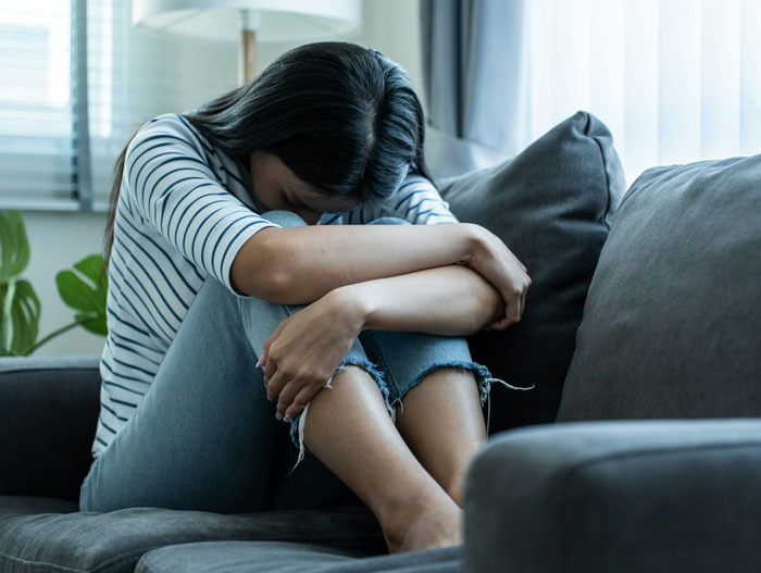 Single mom sitting on couch looking distressed after spending thousands on plastic surgery with no support. Single mom sitting on couch looking distressed after spending thousands on plastic surgery with no support.