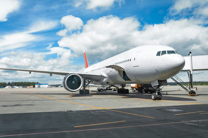 Commercial airplane parked at the gate on the runway with boarding stairs attached under a partly cloudy sky Commercial airplane parked at the gate on the runway with boarding stairs attached under a partly cloudy sky