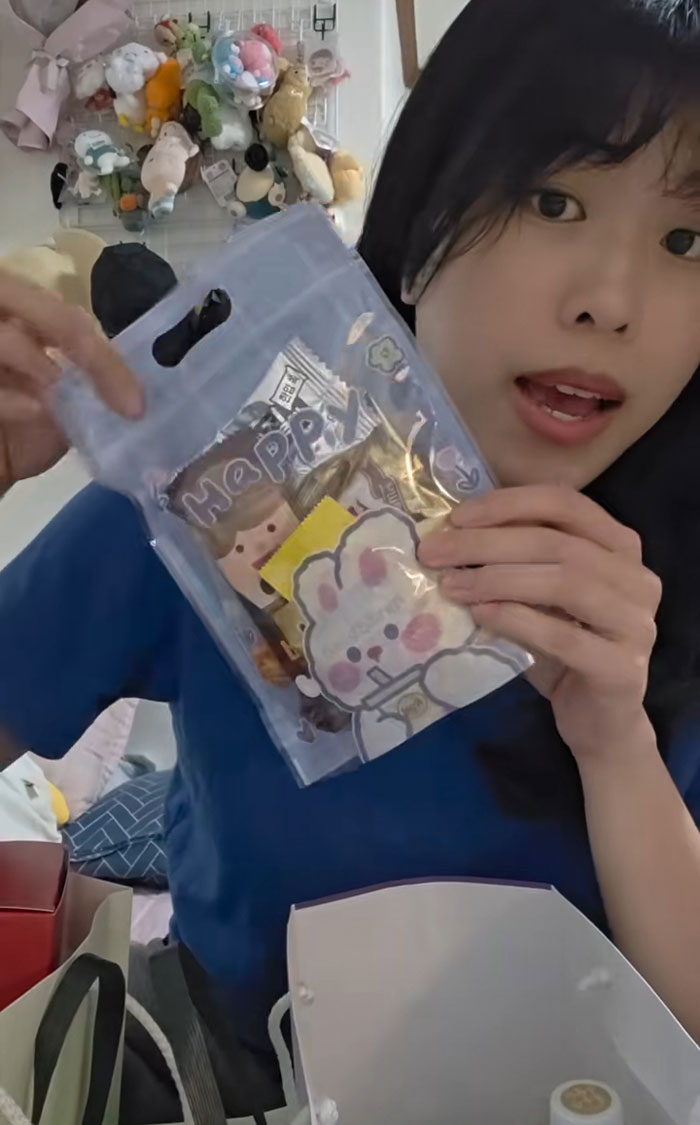 Woman showing cute gift bag and snacks she received during job interview in Korea, surrounded by plush toys and bags. Woman showing cute gift bag and snacks she received during job interview in Korea, surrounded by plush toys and bags.