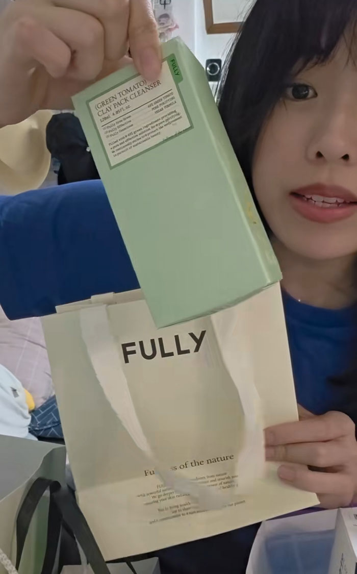 Woman showing gifts received while interviewing for jobs in Korea, holding a green tomato clay pack cleanser and a fully bag. Woman showing gifts received while interviewing for jobs in Korea, holding a green tomato clay pack cleanser and a fully bag.