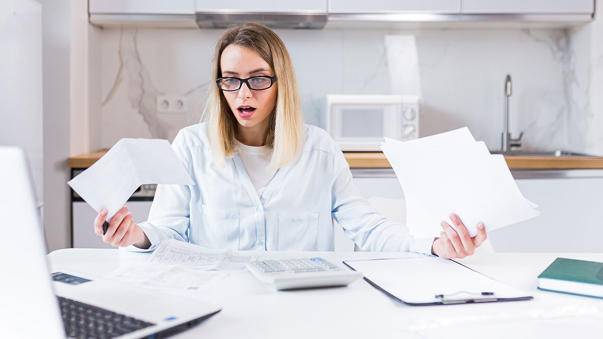 Grieving daughter reviewing bills at kitchen table, showing frustration while dealing with financial ruin paperwork.
