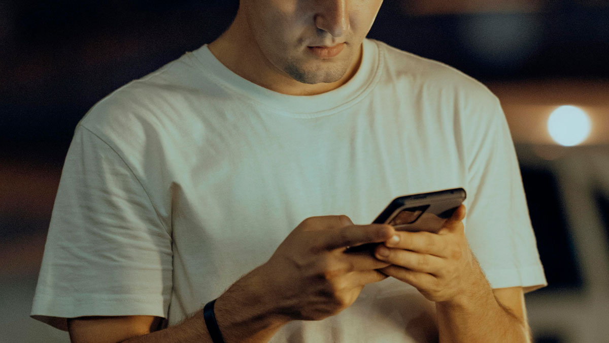 Young man in a white shirt using phone at night, representing creepy men in stories of brutal comebacks by women.