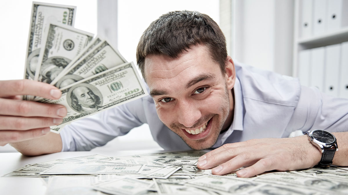Man who won 7 million dollars in the lottery smiling widely while holding cash and surrounded by money on a white table.