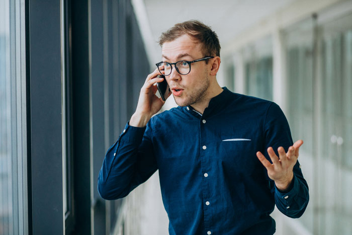 Man in glasses and blue shirt talking on phone in office hallway, showing quiet gossip drama in workplace. Man in glasses and blue shirt talking on phone in office hallway, showing quiet gossip drama in workplace.
