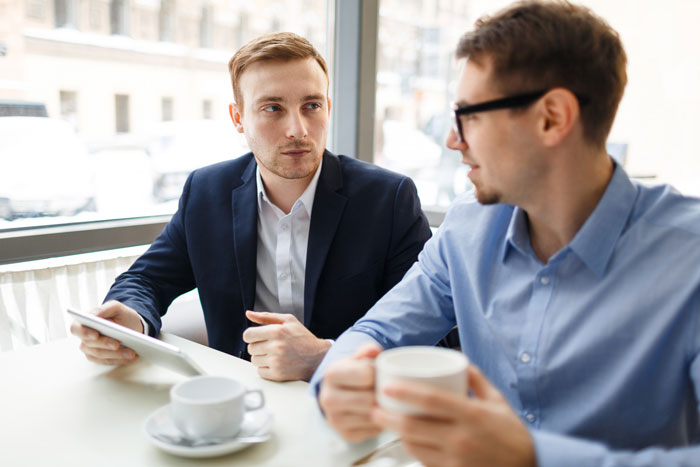 Two young men having a quiet work conversation over coffee, possibly discussing gossip or drama during a break. Two young men having a quiet work conversation over coffee, possibly discussing gossip or drama during a break.