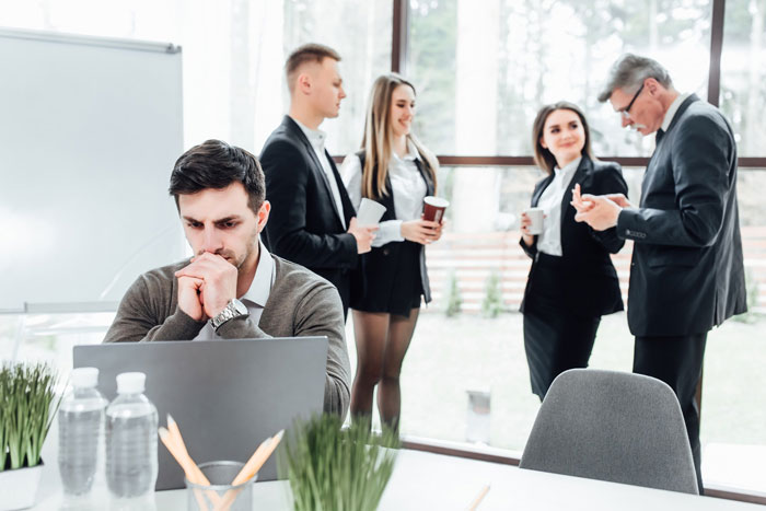 Man working quietly on laptop in office while coworkers engage in gossip and drama behind him. Man working quietly on laptop in office while coworkers engage in gossip and drama behind him.
