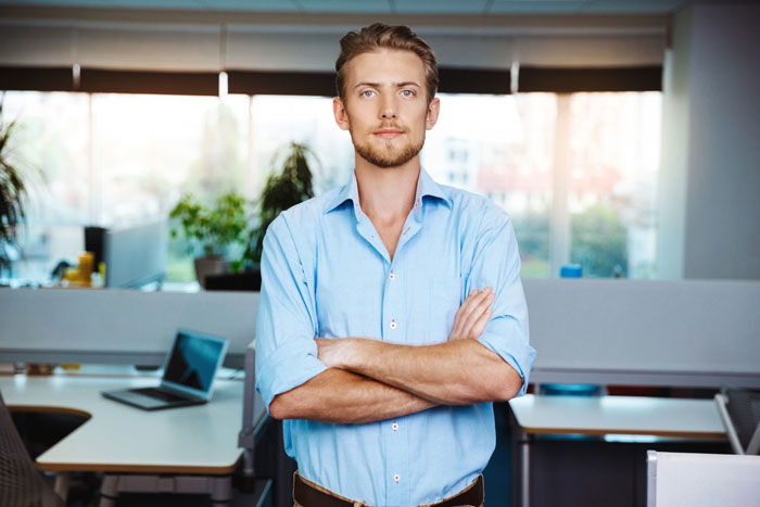 Young man standing with arms crossed in a modern office, embodying work quiet focus away from gossip and drama. Young man standing with arms crossed in a modern office, embodying work quiet focus away from gossip and drama.