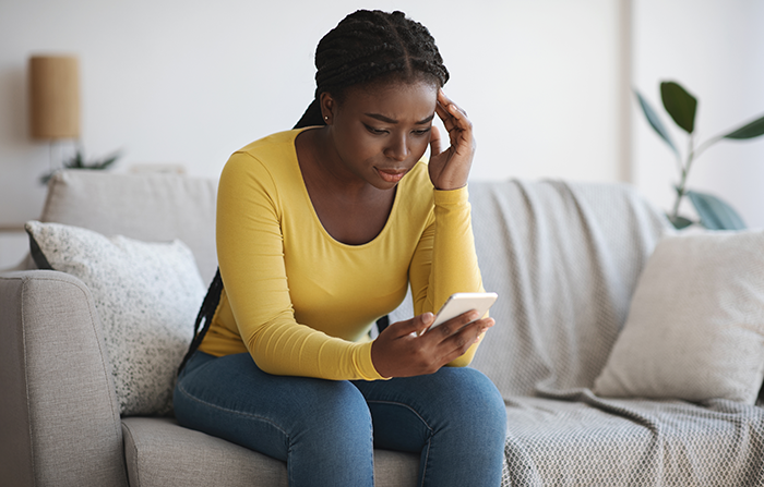 Woman sitting on couch looking worried at phone, suspecting the guy she's seeing is lying about medical school.