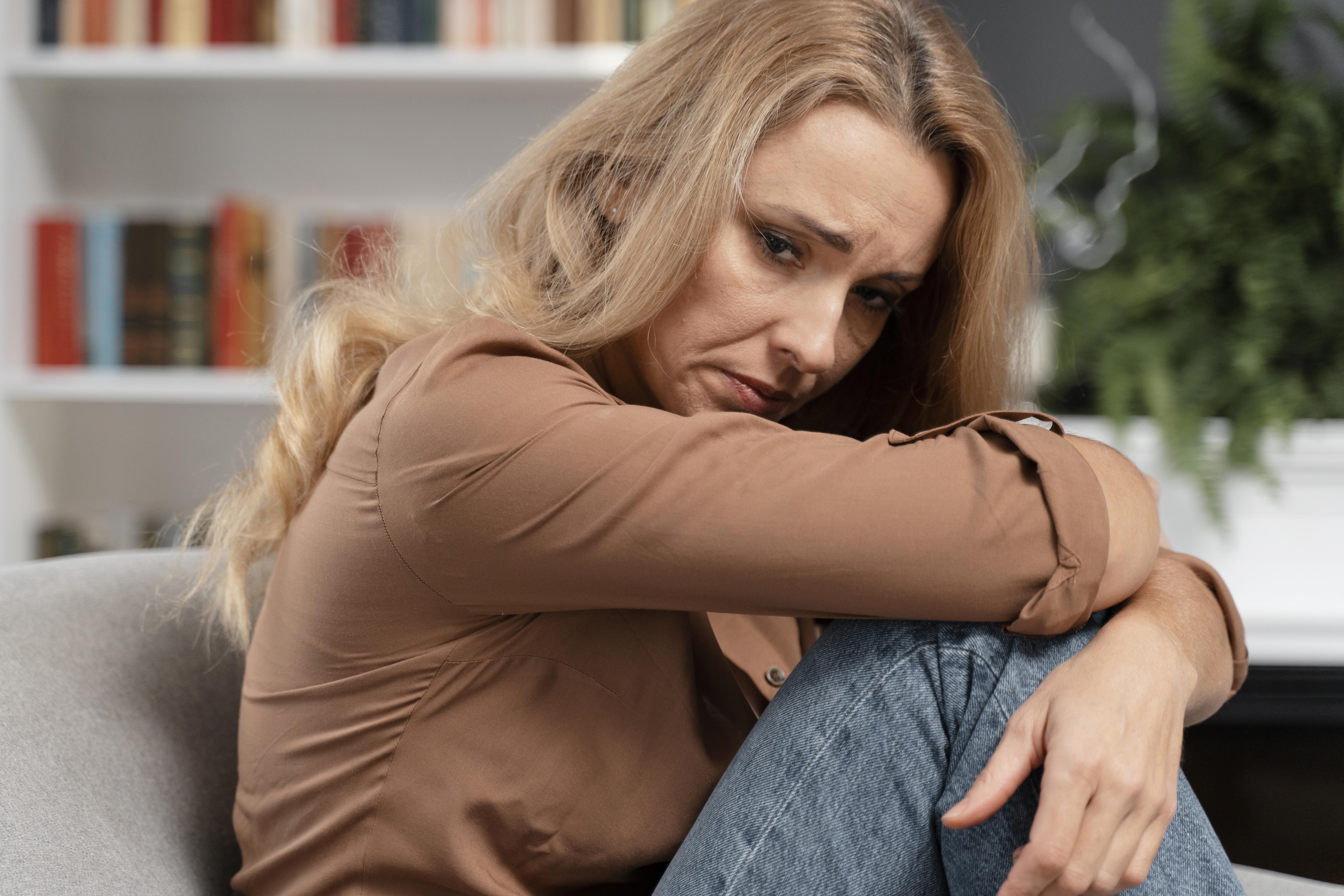 Sad woman sitting with arms wrapped around knees, reflecting on mom and daughter estrangement after harsh words. Sad woman sitting with arms wrapped around knees, reflecting on mom and daughter estrangement after harsh words.