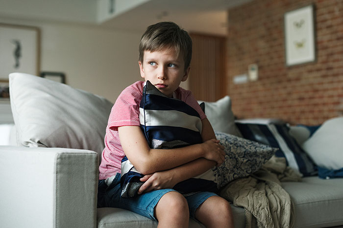 Boy babysitter hugging a pillow on a couch, capturing a weird and awkward babysitting moment indoors.