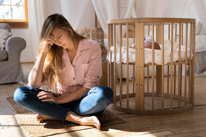 Babysitter sitting on floor looking stressed next to crib, reflecting on weird and awkward babysitting moments.