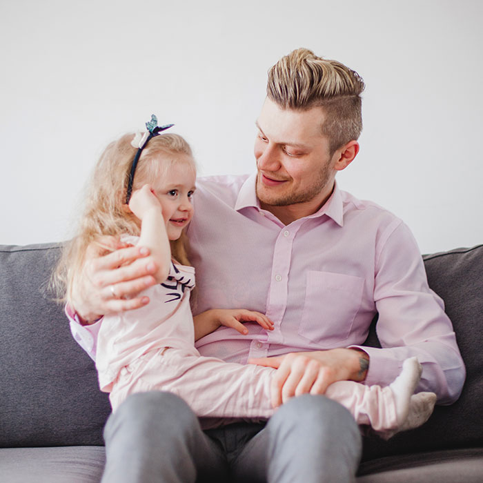 Young babysitter holding a little girl on his lap, sharing a warm moment during babysitting duties at home.