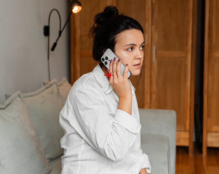 Woman babysitter in casual attire talking on phone, reflecting on awkward and weird babysitting moments at home.