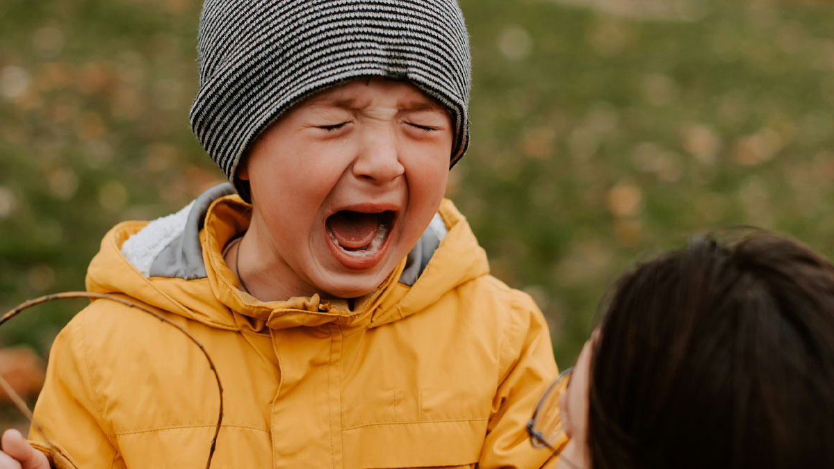 Young boy in yellow jacket and striped hat crying outdoors, capturing emotional moments in worst funeral stories context