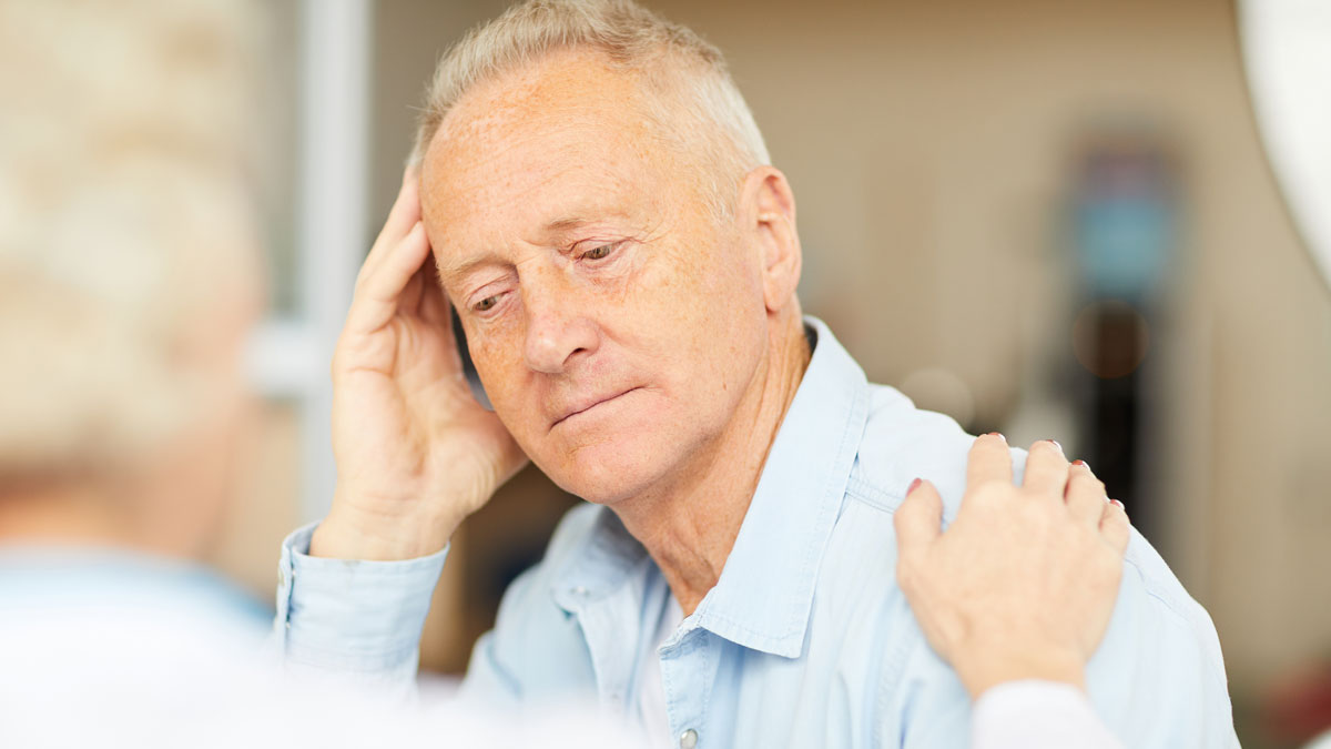 Elderly man looking distressed while being comforted, illustrating doctors revealing dangerous medical mistakes to fix.