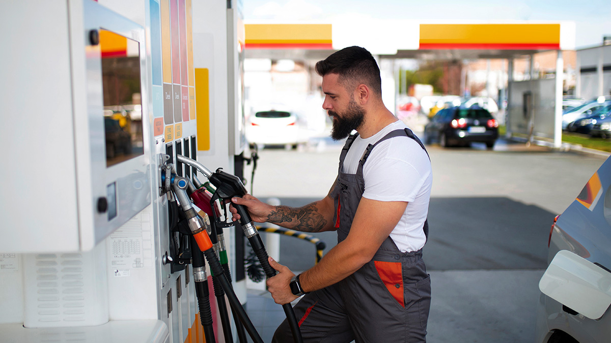 Man in work uniform struggling to use the wrong gas pump hose at a busy fuel station during work hours