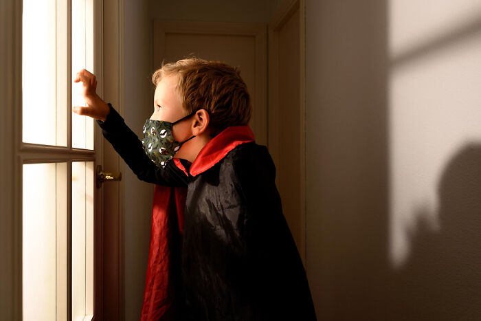 Child in a Halloween costume wearing a face mask, looking out a window, capturing a spooky and nightmare Halloween experience.