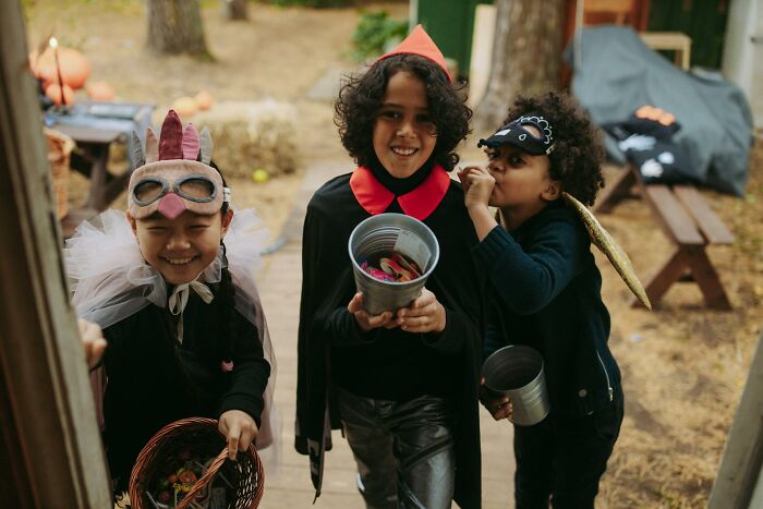 Three children wearing Halloween costumes holding buckets of candy during trick-or-treating Halloween experiences.