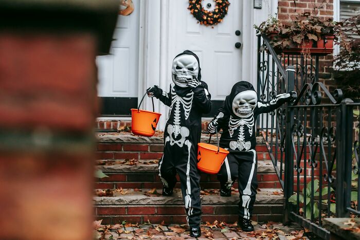 Two children in skeleton Halloween costumes holding orange buckets walking down outdoor steps at night.
