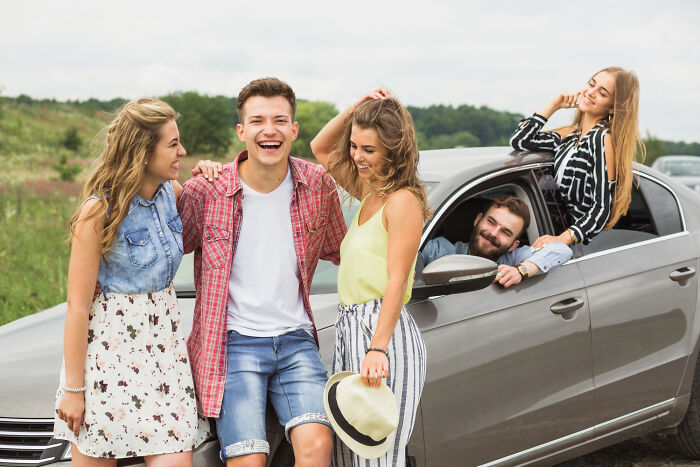 Group of young friends laughing and hanging out near a car, sharing memorable worst Halloween experiences together.