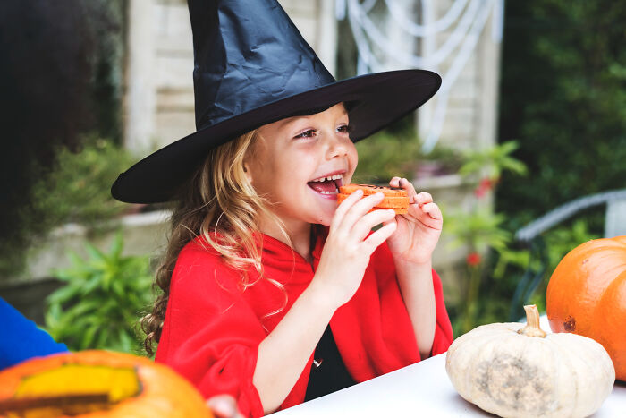 Young girl in a witch costume enjoying Halloween treats surrounded by pumpkins and festive decorations outdoors