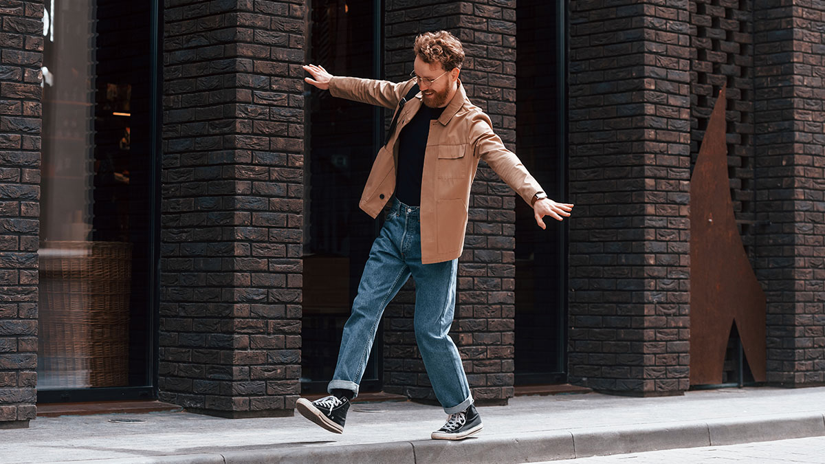 Man walking playfully on a city sidewalk, dressed casually, illustrating myths about men that are simply not true.