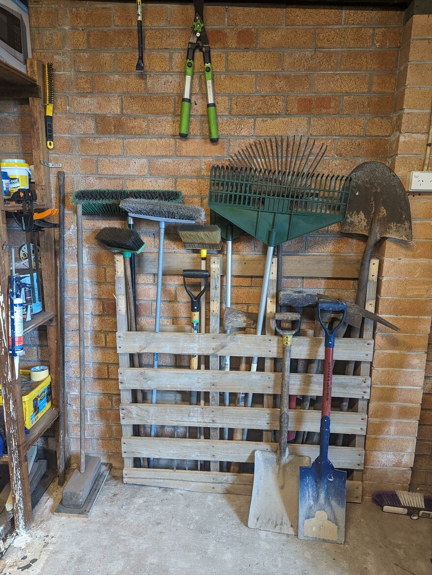 Organized garden tools neatly stored against a brick wall using a wooden pallet for efficient home organization hacks.