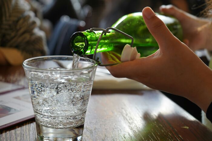 Waiter pouring water from a green bottle into a glass, illustrating a painful table for two moment ending with table for one.